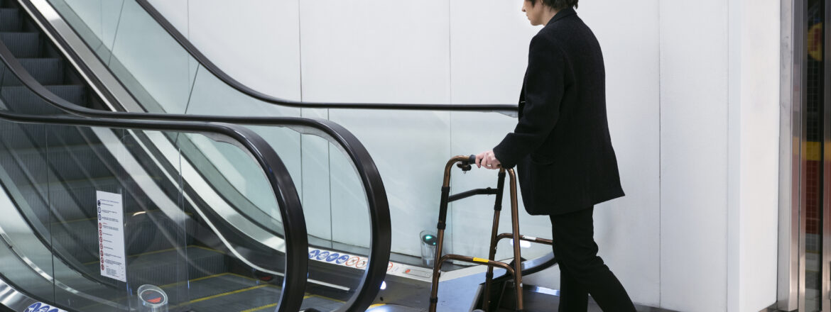 An adult with a walking frame near escalators, emphasizing the need for accessible and safe vertical mobility solutions.