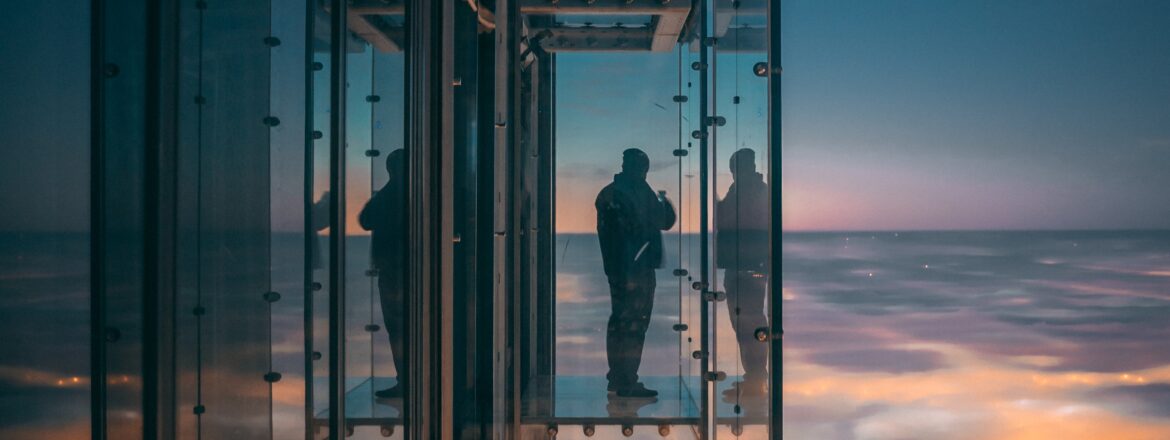 A person enjoying a breathtaking city view from a panoramic lift with glass walls in a tall skyscraper.